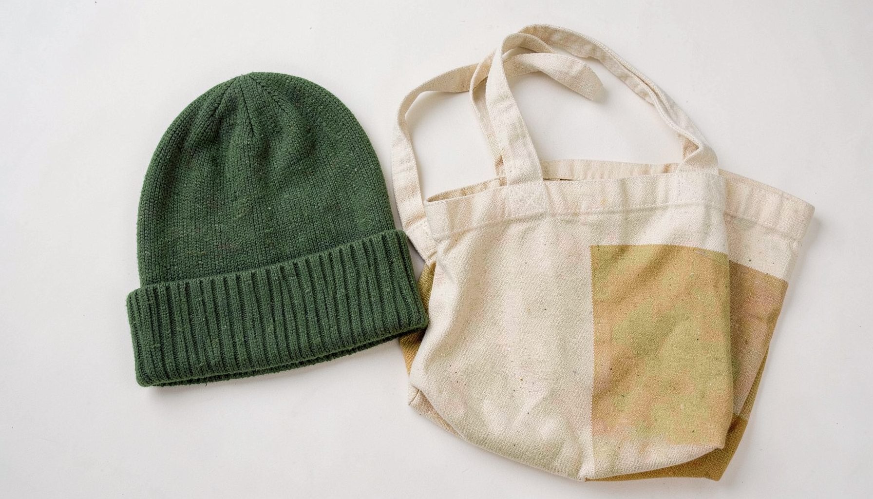 A woolen beanie hat and a canvas tote bag in green and amber tones laid flat